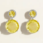 Pair of festive large yellow lemon quartz gemstone earrings with diamond halo on a beige background