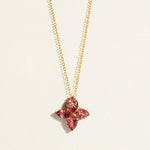 Gold chain with a peach pink tourmalines in flower-shaped pendant on a light background