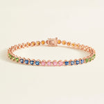 Rose gold tennis bracelet with rainbow sapphires on a light beige background