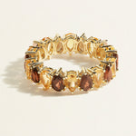 Gold eternity ring with brown pear smoky quartz and pear yellow citrine gemstones on a light beige background