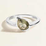 white gold ring with a green gray tourmaline pear gemstone on a light beige background