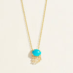 14 k Closer Gold necklace with a natiral turquoise pendant with hanging pearls on a light beige background