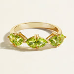 Gold stacking ring with green peridot gemstones on a light beige background