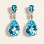 Pair of cocktail gold blue topaz teardrop earrings in gold on a light beige background
