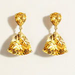 Pair of yellow citrine drop gemstone in gold earrings on a light beige background