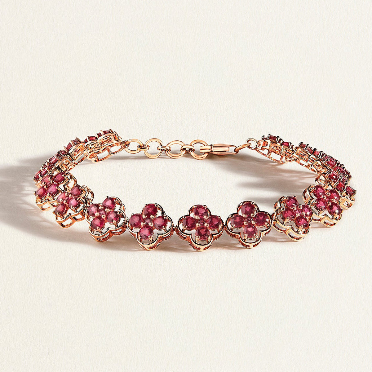 Rose gold bracelet with pink rhodolites gemstones on a light beige background