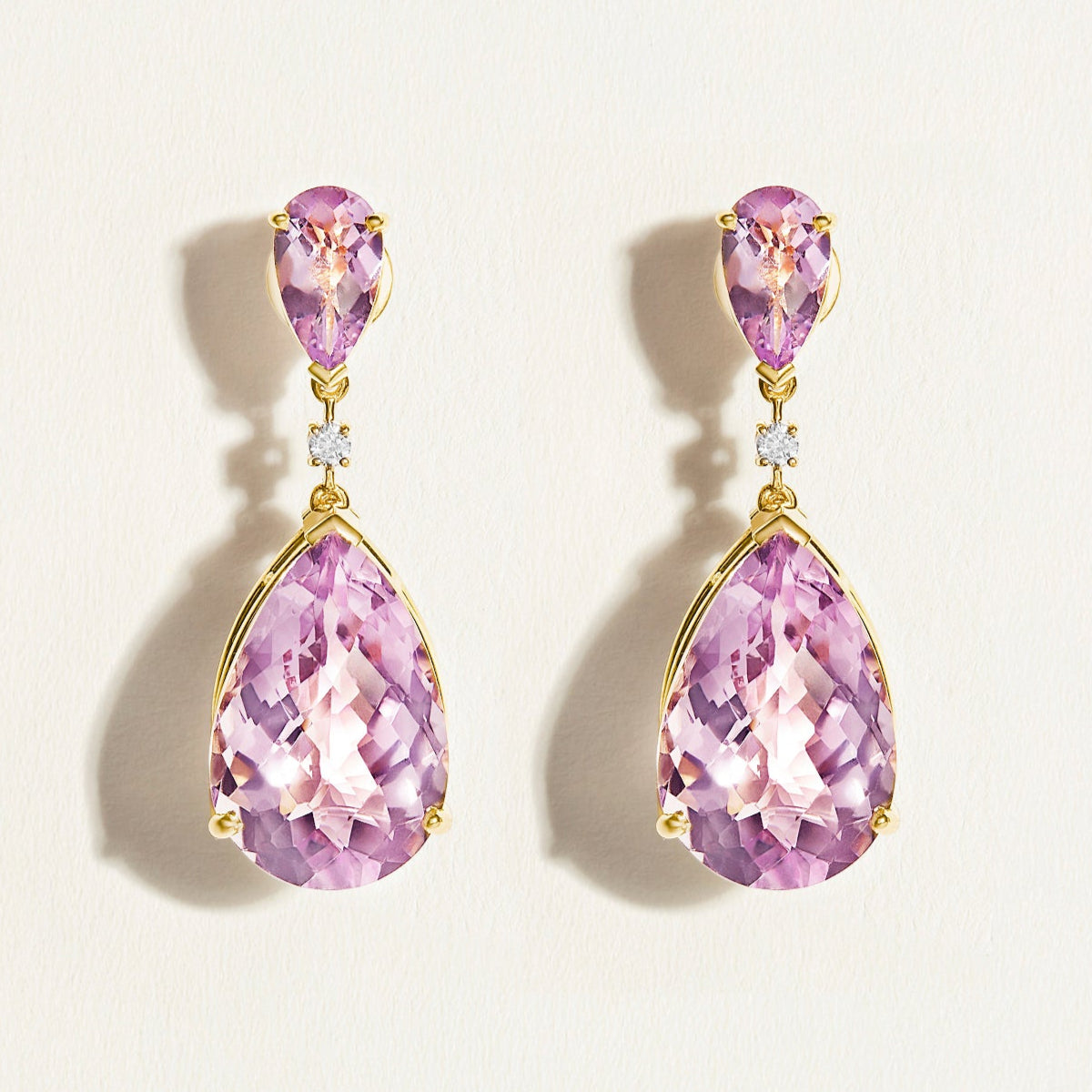 Pair of statement festive light purple amethysts large teardrop earrings in 14 k gold with diamonds on a light beige background