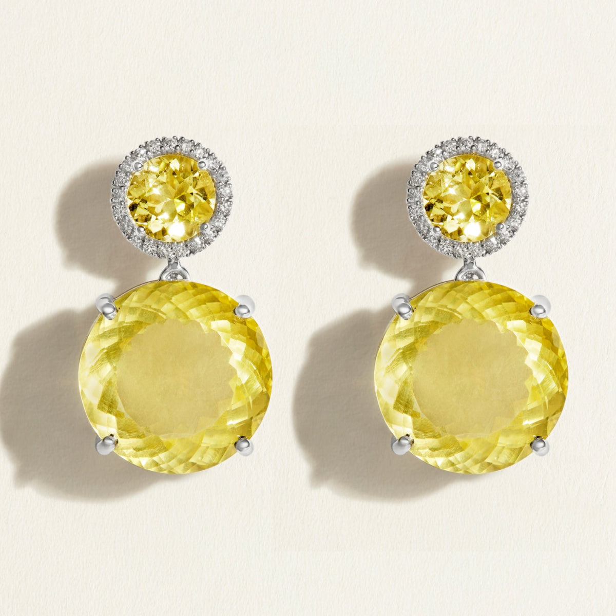 Pair of festive large yellow lemon quartz gemstone earrings with diamond halo on a beige background