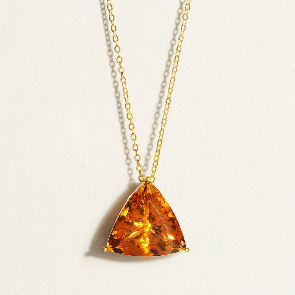 Trillion large amber brandy citrine pendant on a 14k 18k gold chain against a light background