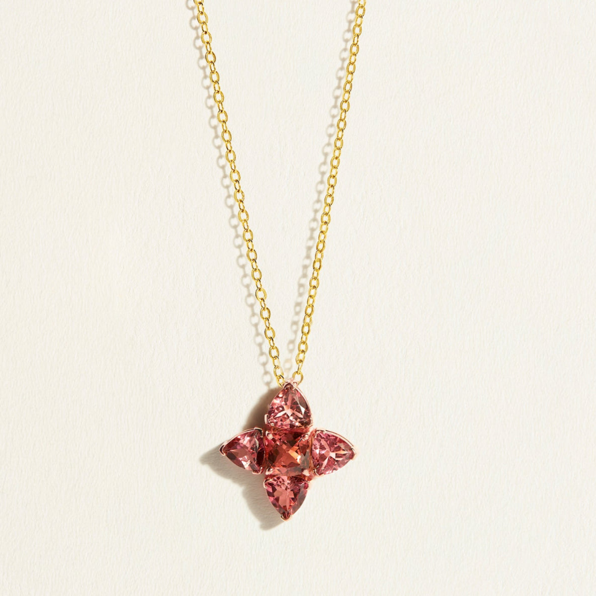 Gold chain with a peach pink tourmalines in flower-shaped pendant on a light background