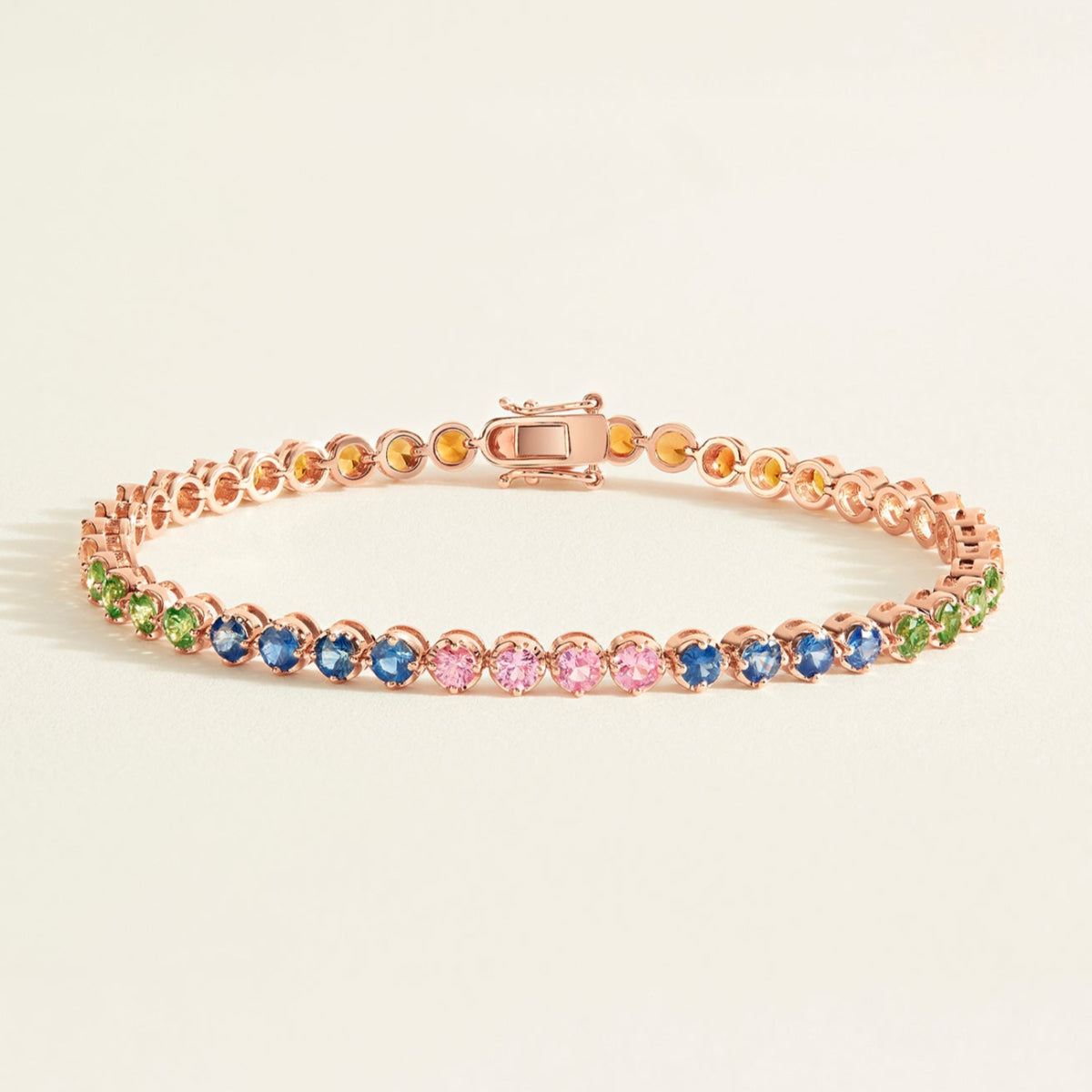 Rose gold tennis bracelet with rainbow sapphires on a light beige background