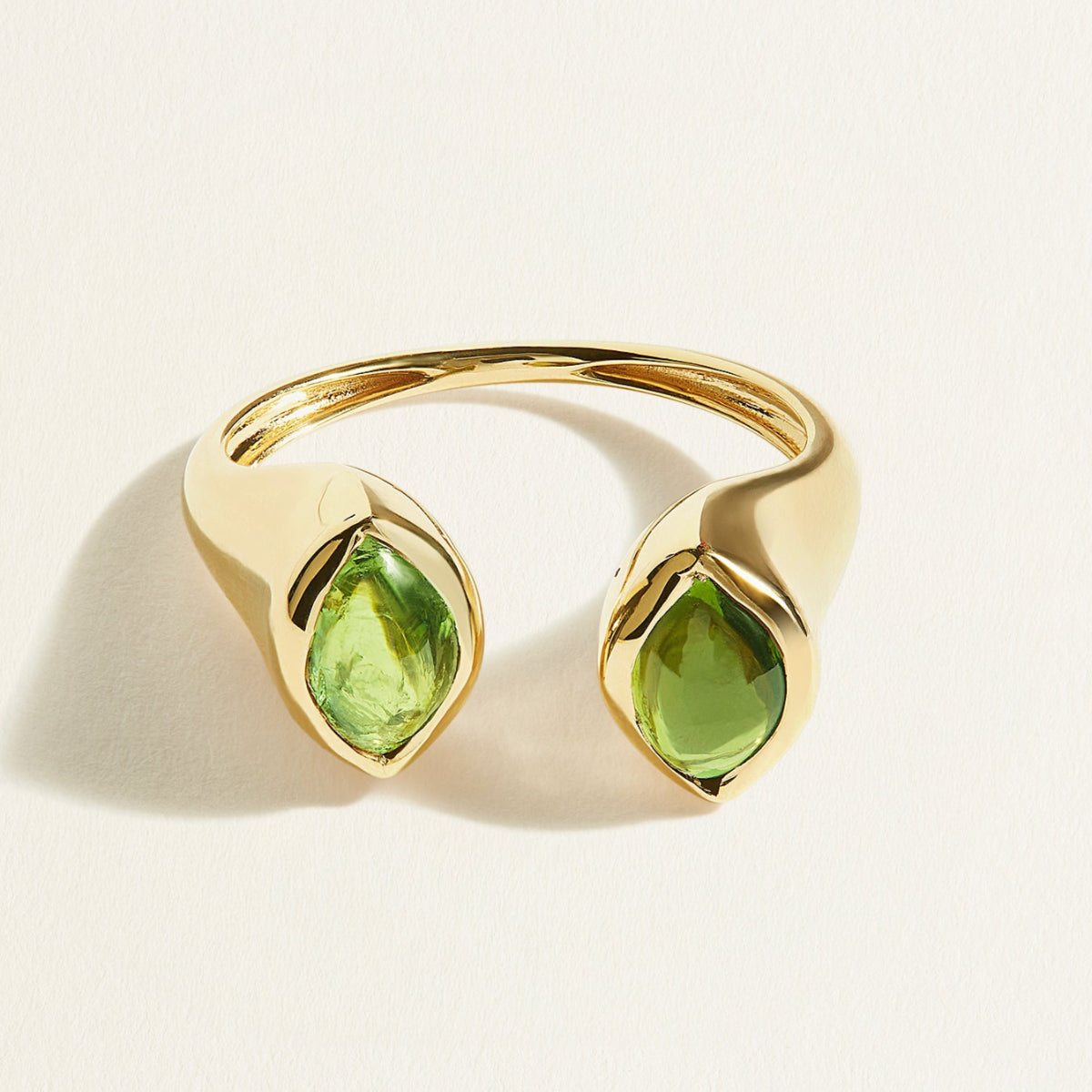 Gold signet ring with green cabochon tourmaline gemstones on a light beige background