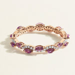Rose gold eternity ring with diamond wave band with purple amethyst gemstones on a light beige background