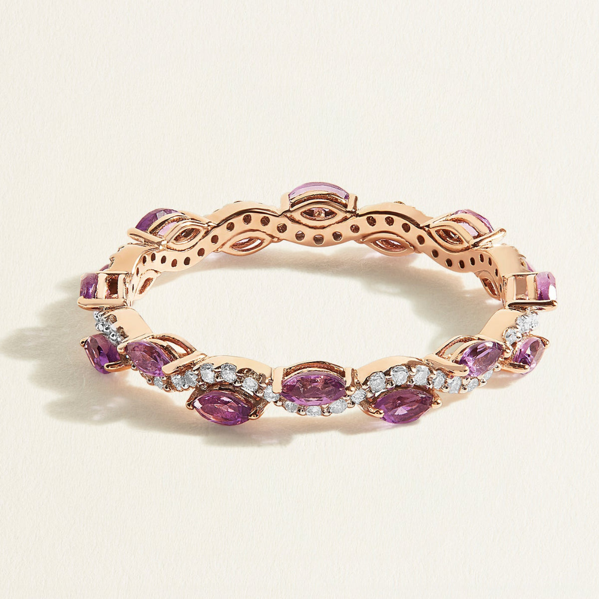 Rose gold eternity ring with diamond wave band with purple amethyst gemstones on a light beige background