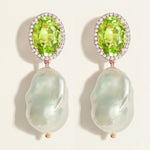 Pair of statement earrings with oval green peridot gemstones with diamond halo  and  baroque pearl drops on a light background