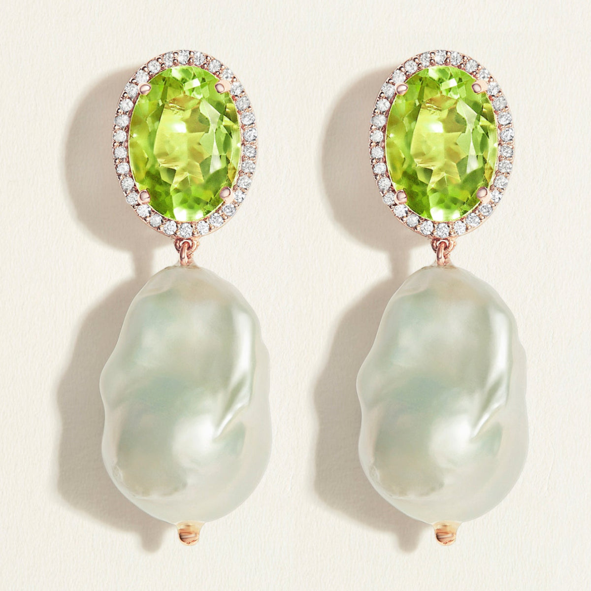 Pair of statement earrings with oval green peridot gemstones with diamond halo  and  baroque pearl drops on a light background