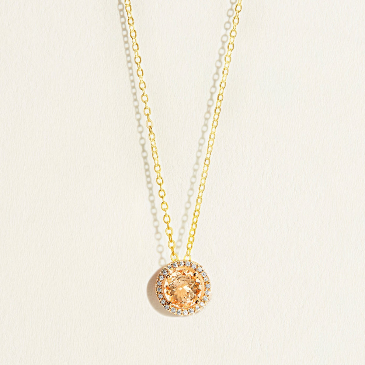 14 k Gold  everyday necklace with a round peach morganite pendant with diamond halo on a light beige background