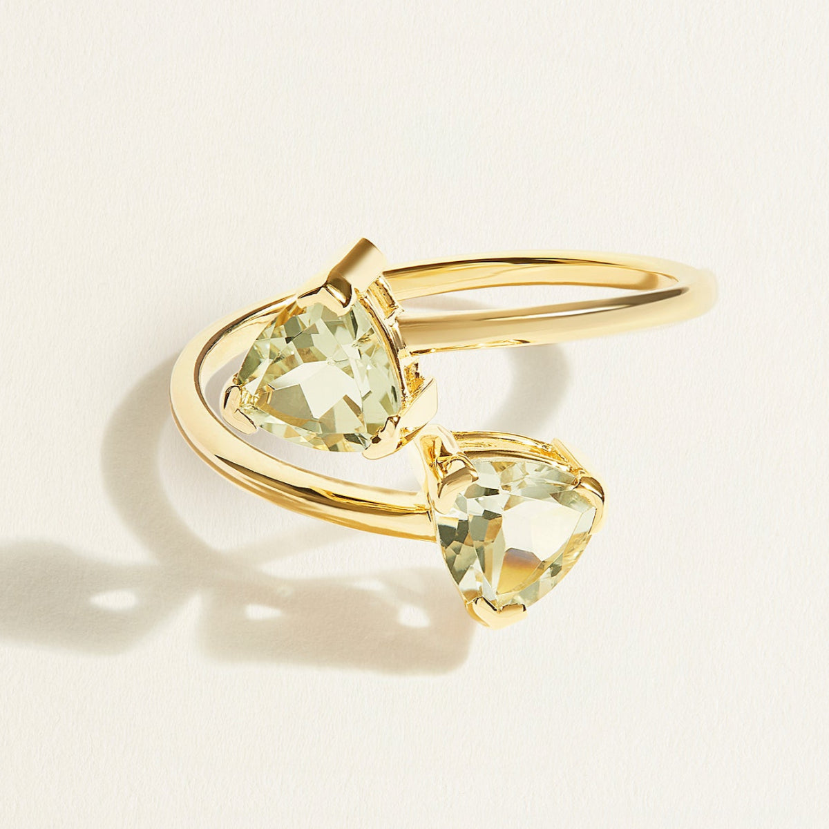 14 k Gold toi et moi ring with two green trillion amethyst gemstones on a light beige background