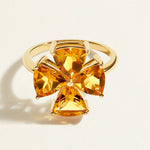 Gold ring with four yellow citrines gemstones in a clover pattern on a light beige background