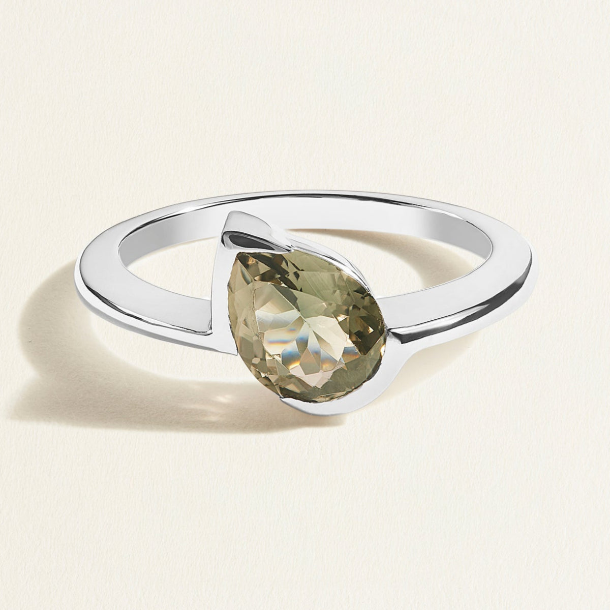 white gold ring with a green gray tourmaline pear gemstone on a light beige background