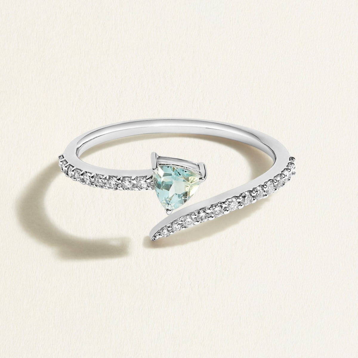 White gold diamond spiral ring with a triangular light blue aquamarine gemstone on a light beige background