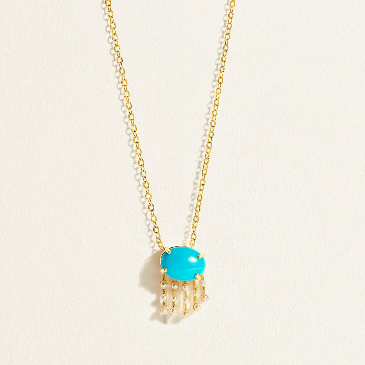 14 k Closer Gold necklace with a natiral turquoise pendant  with hanging pearls on a light beige background