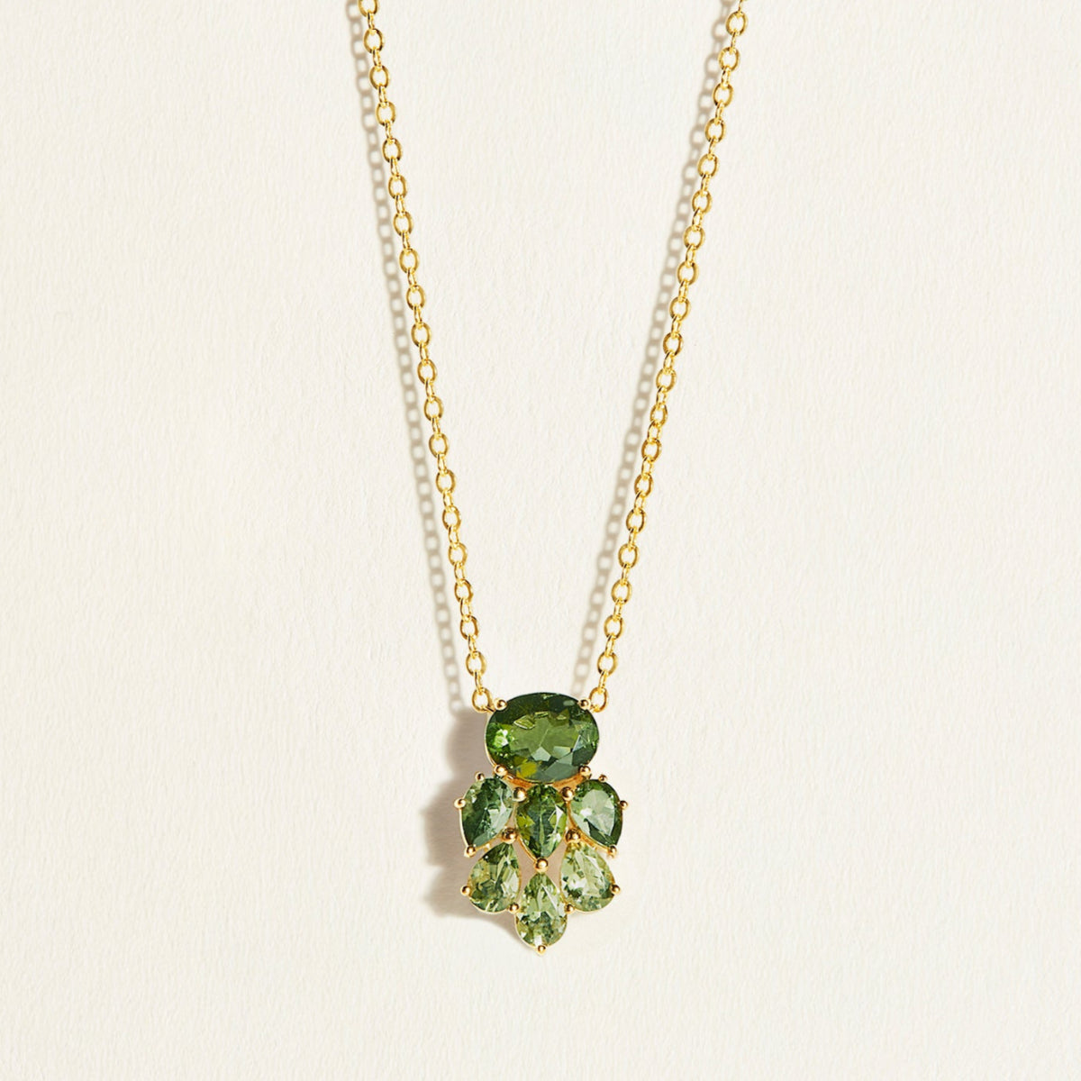 14k Gold chain necklace with green tourmaline gemstones on a light beige background