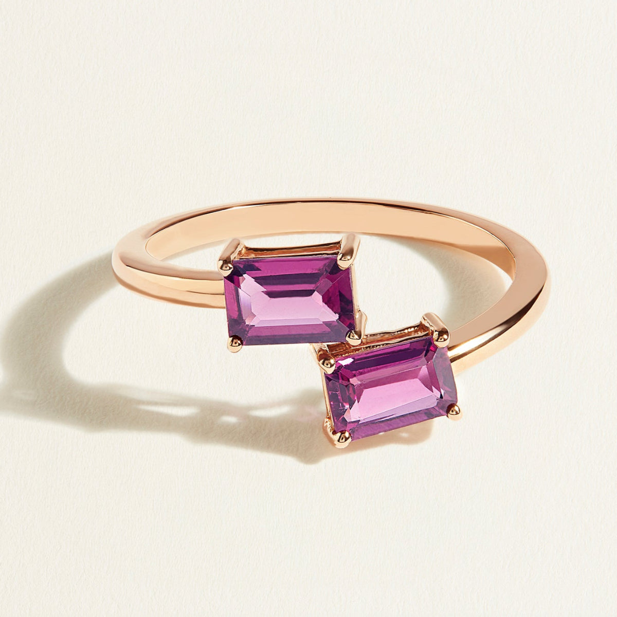 Rose gold  toi et moi ring with two pink rhodolite gemstones on a light beige background