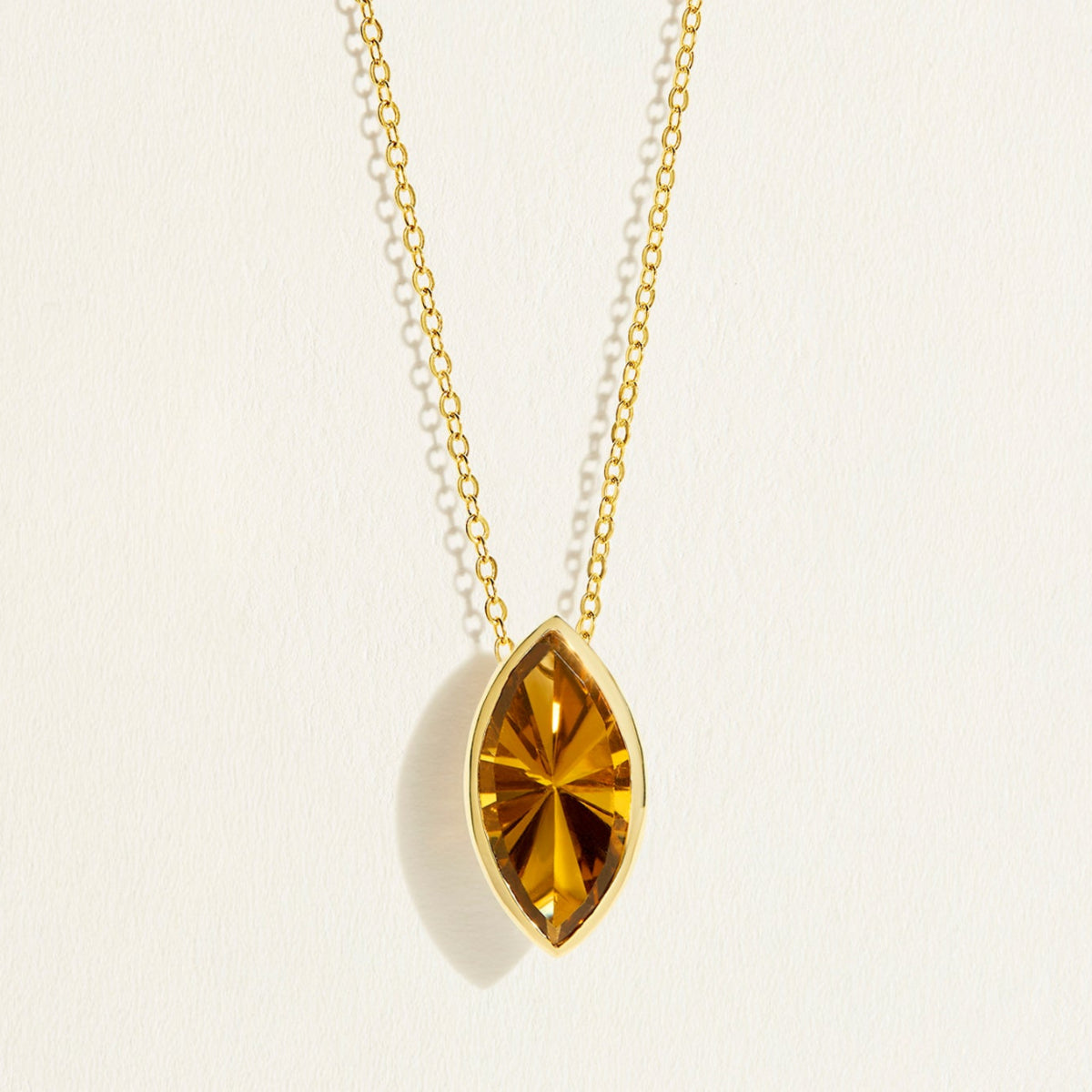 14/18 karat Gold chain necklace with a large marquise-shaped dark yellow olive quartz gemstone pendant on a light background