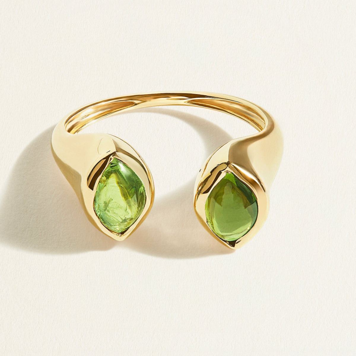 Gold signet ring with green cabochon tourmaline gemstones on a light beige background