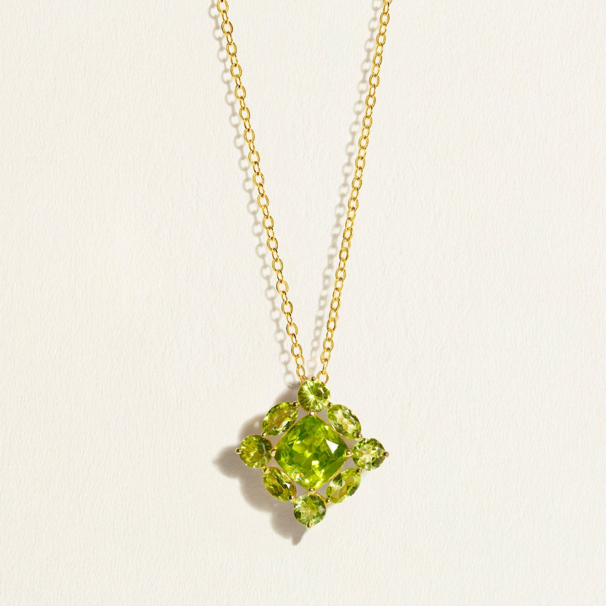 14 k 18 k Gold chain necklace with a green peridot cluster gemstone pendant on a light beige background