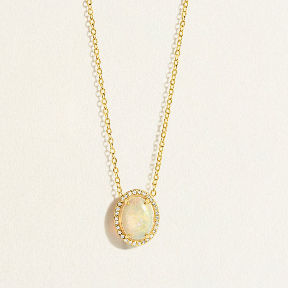14k Gold everyday chain necklace with an opal pendant with diamond halo on a light beige background