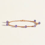 Gold bracelet with purple blue tanzanite beads on a light beige background