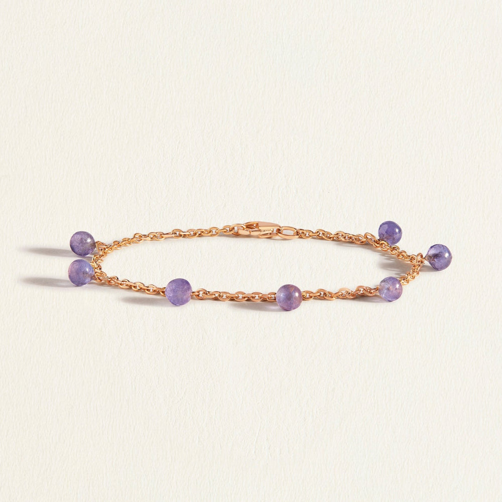 Gold bracelet with purple blue tanzanite beads on a light beige background