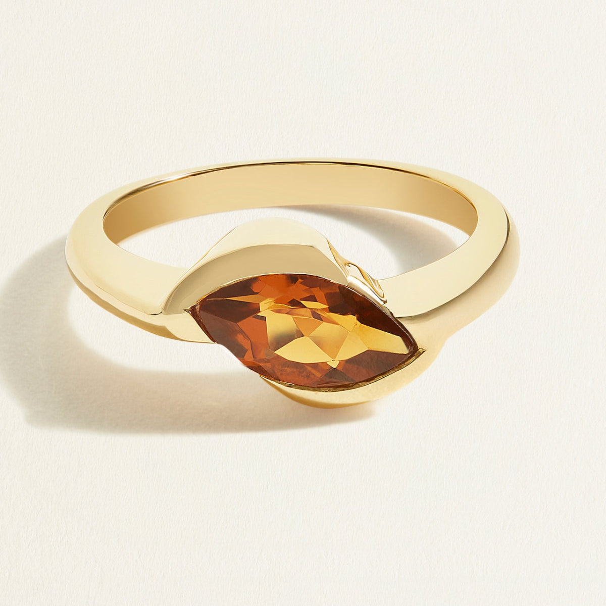 Gold ring with a brown marquise bear quartz gemstone on a light beige background