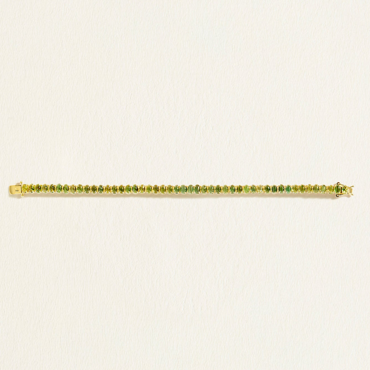 14 k Gold tennis bracelet with green oval tourmaline gemstones on a light beige background