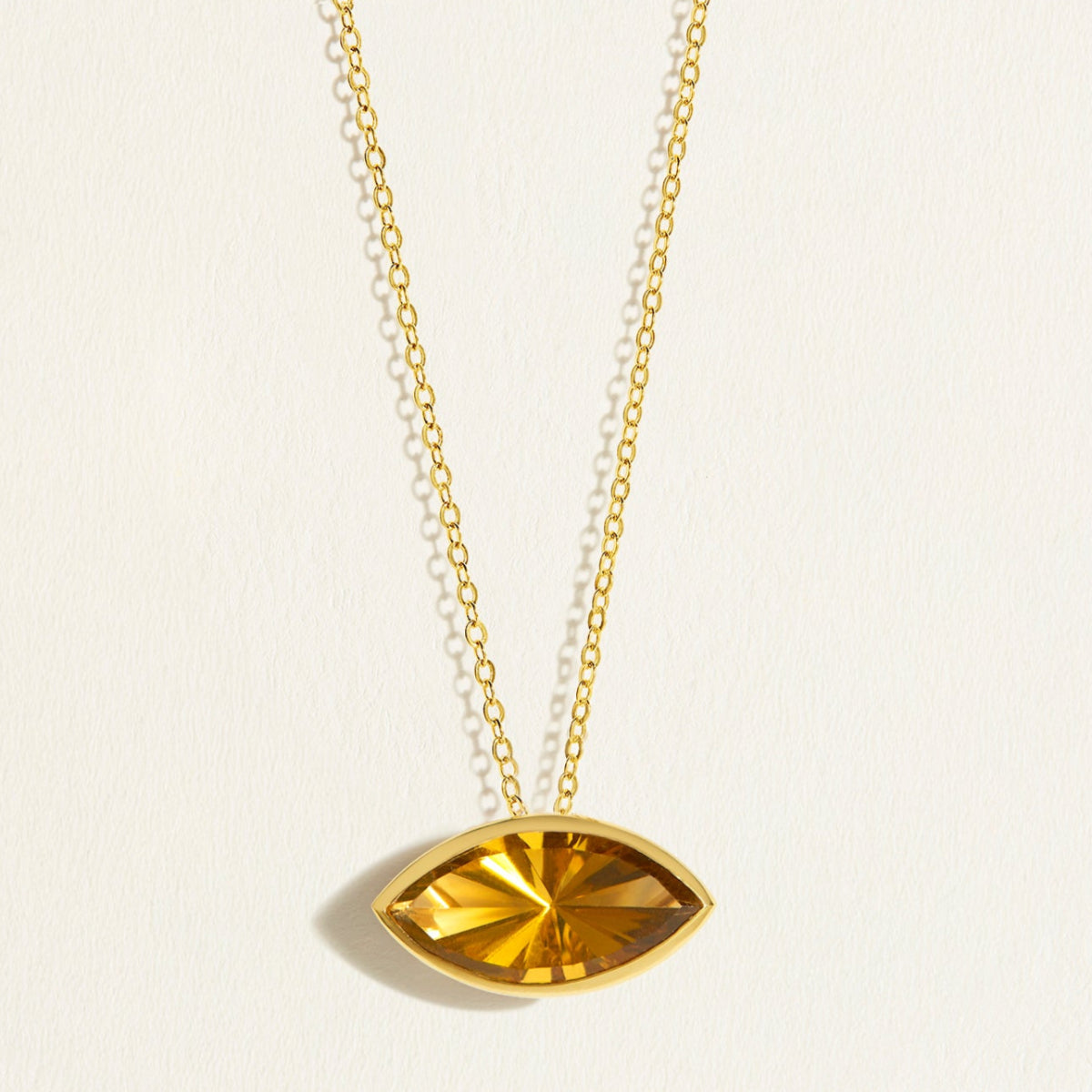 Gold chain necklace with a deep yellow east west setting olive quartz gemstone pendant on a light beige background