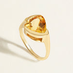 14/18k k Gold solitaire ring with a large trillion yellow citrine gemstone on a light beige background