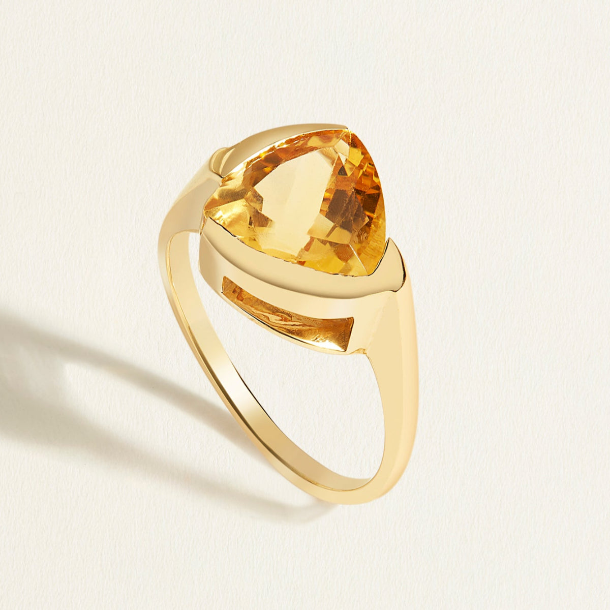 14/18k k Gold solitaire ring with a large trillion yellow citrine gemstone on a light beige background