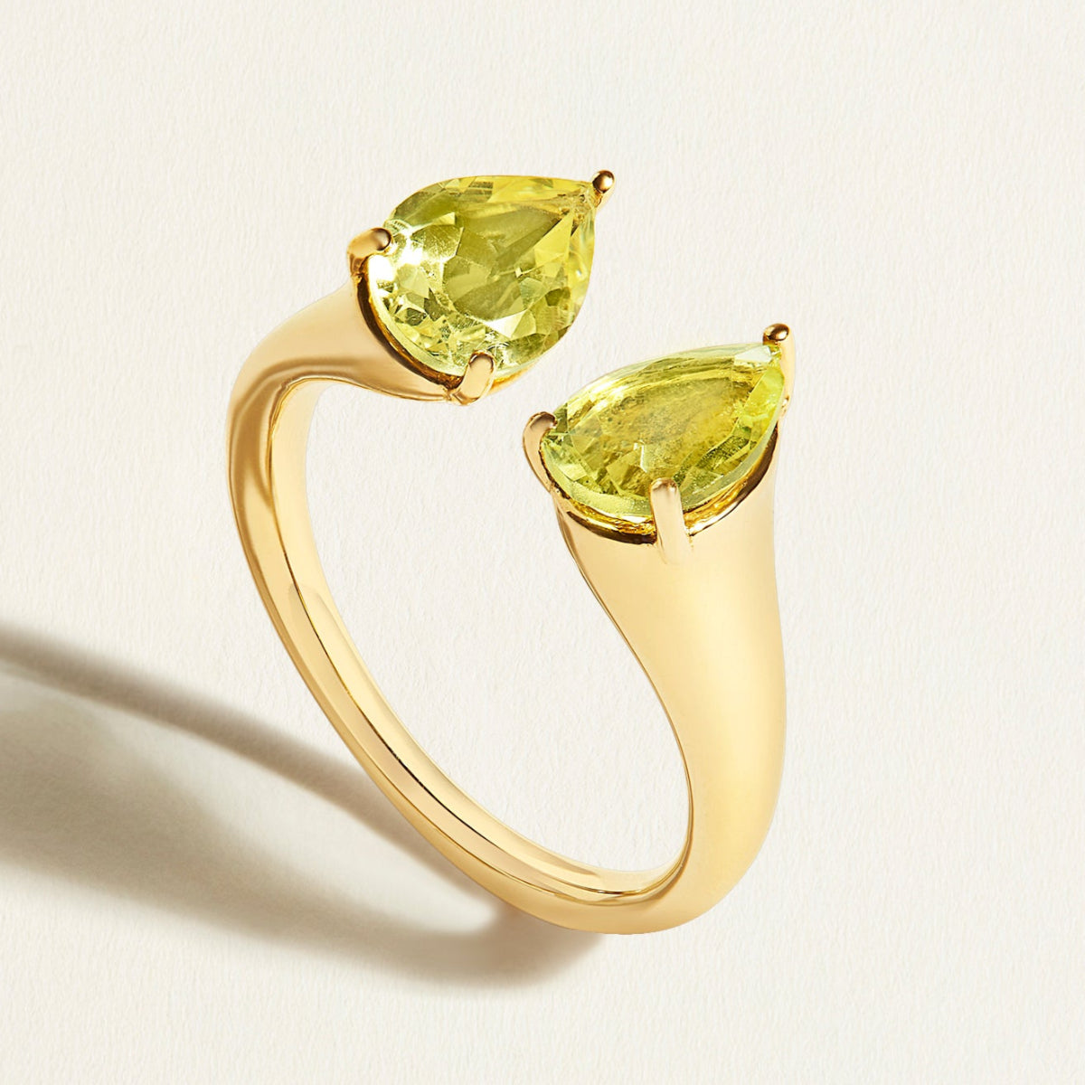 Gold open signet ring with two pear-shaped yellow lemon quartz gemstones on a light background