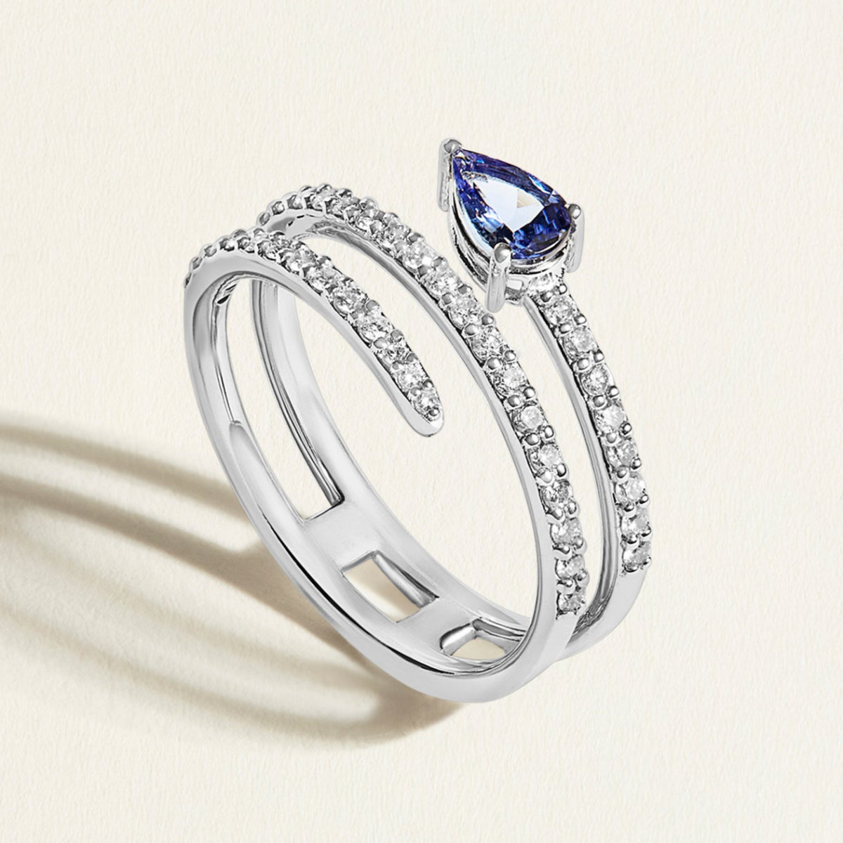 white gold spiral  diamond ring with a purple blue tanzanite gemstone on a light beige background