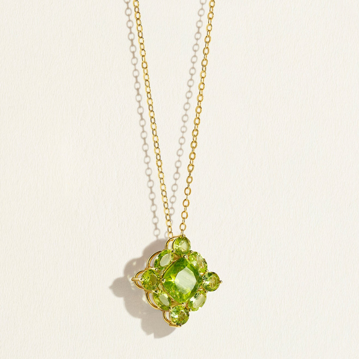 14 k Gold chain necklace with a green peridot cluster gemstone designer pendant on a light beige background