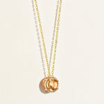 Gold minimal necklace with a circular morganite peach pendant with diamond halo on a light beige background