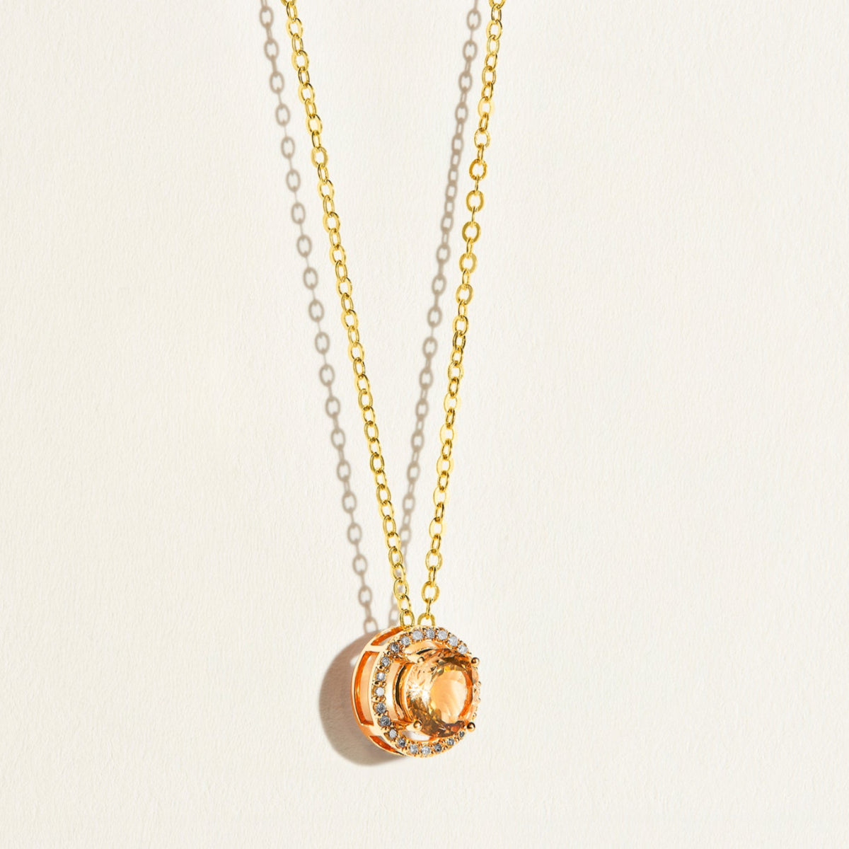 Gold minimal necklace with a circular morganite peach pendant with diamond halo on a light beige background