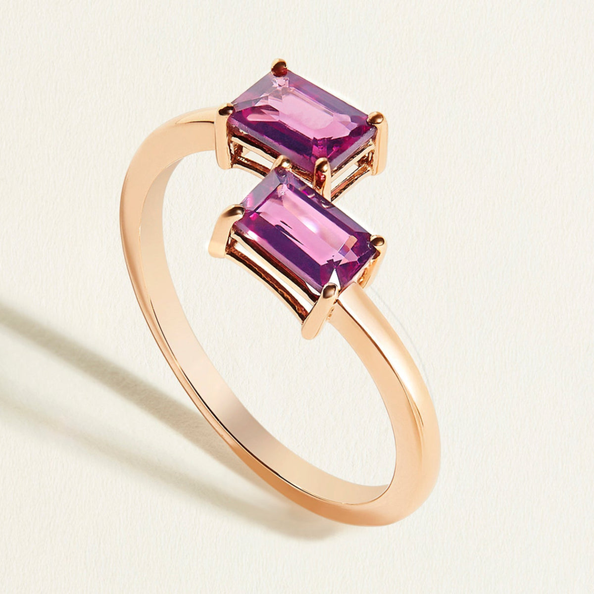 Rose gold  toi et moi ring with two pink rhodolite gemstones on a light beige background
