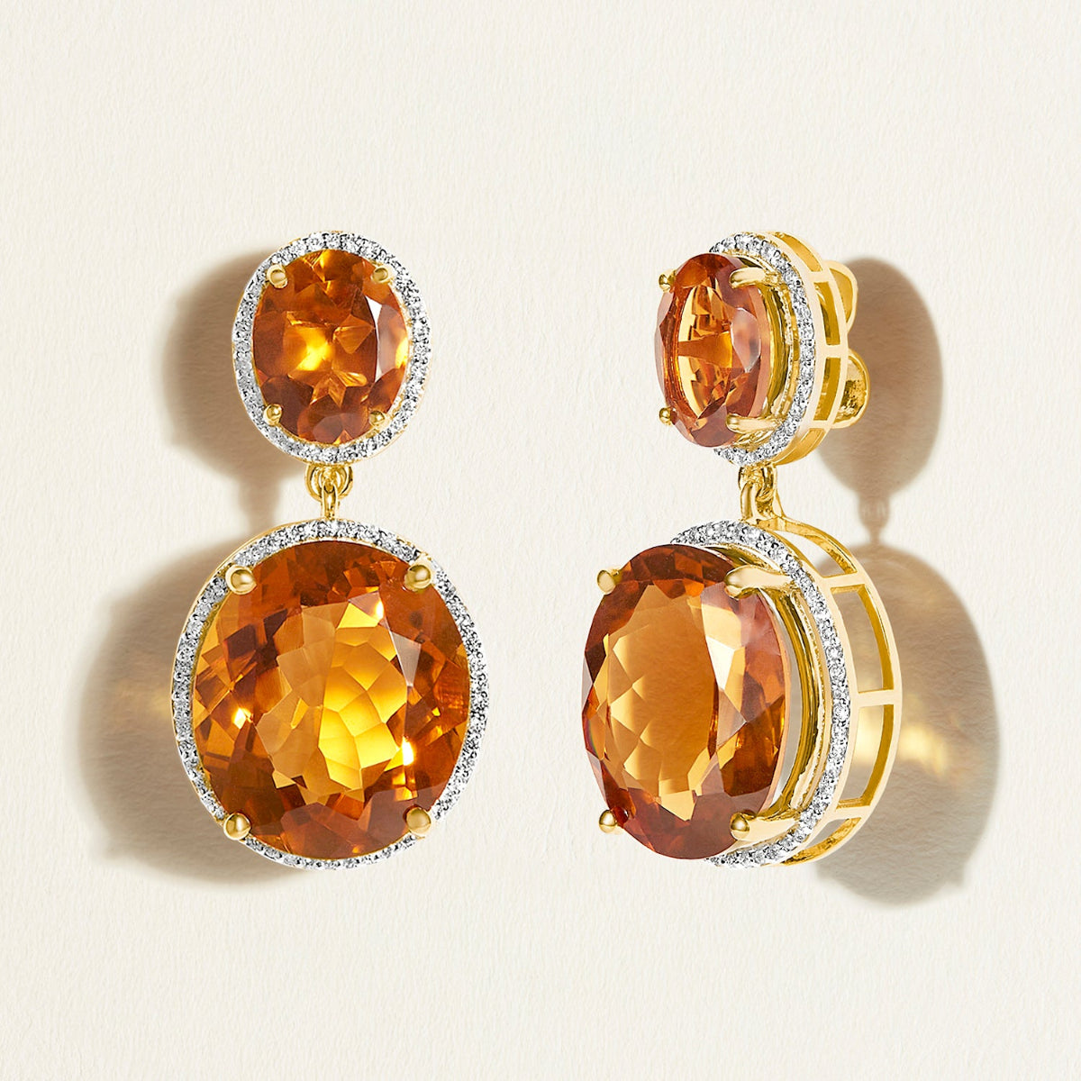 Pair of gold luxury statement earrings with large orange gemstones and diamond halo on a beige background