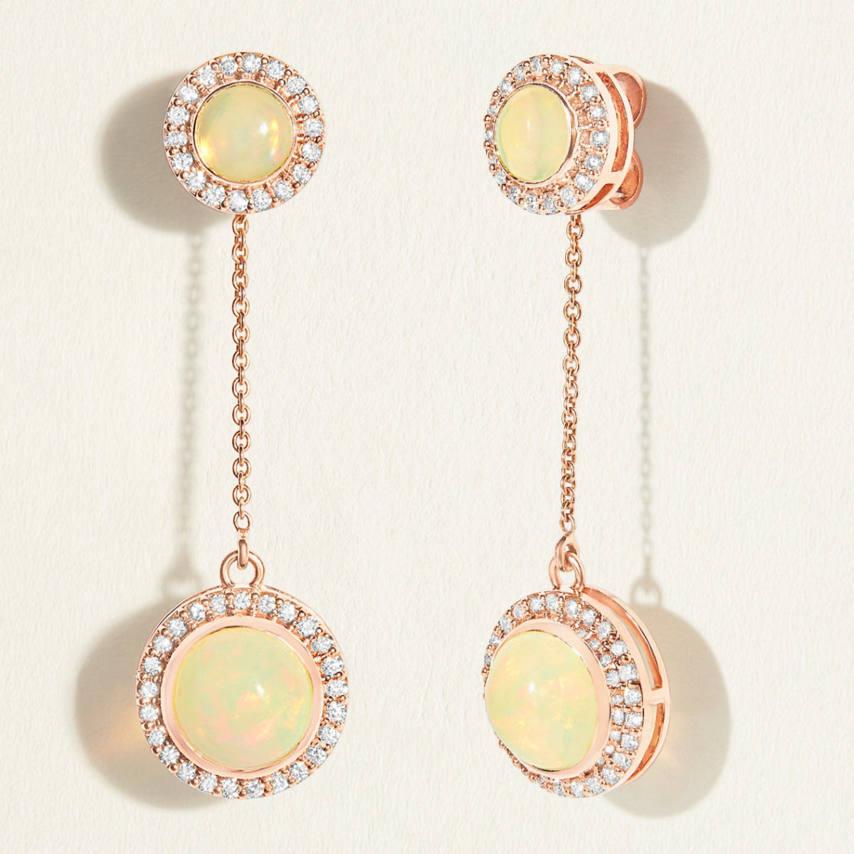 Pair of rose gold 18k earrings with opal stones and rose gold accents with diamond halo on a light background