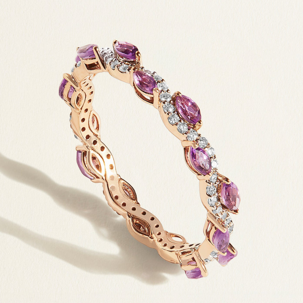 Rose gold diamond wave eternity ring with purple amethyst gemstones on a light background