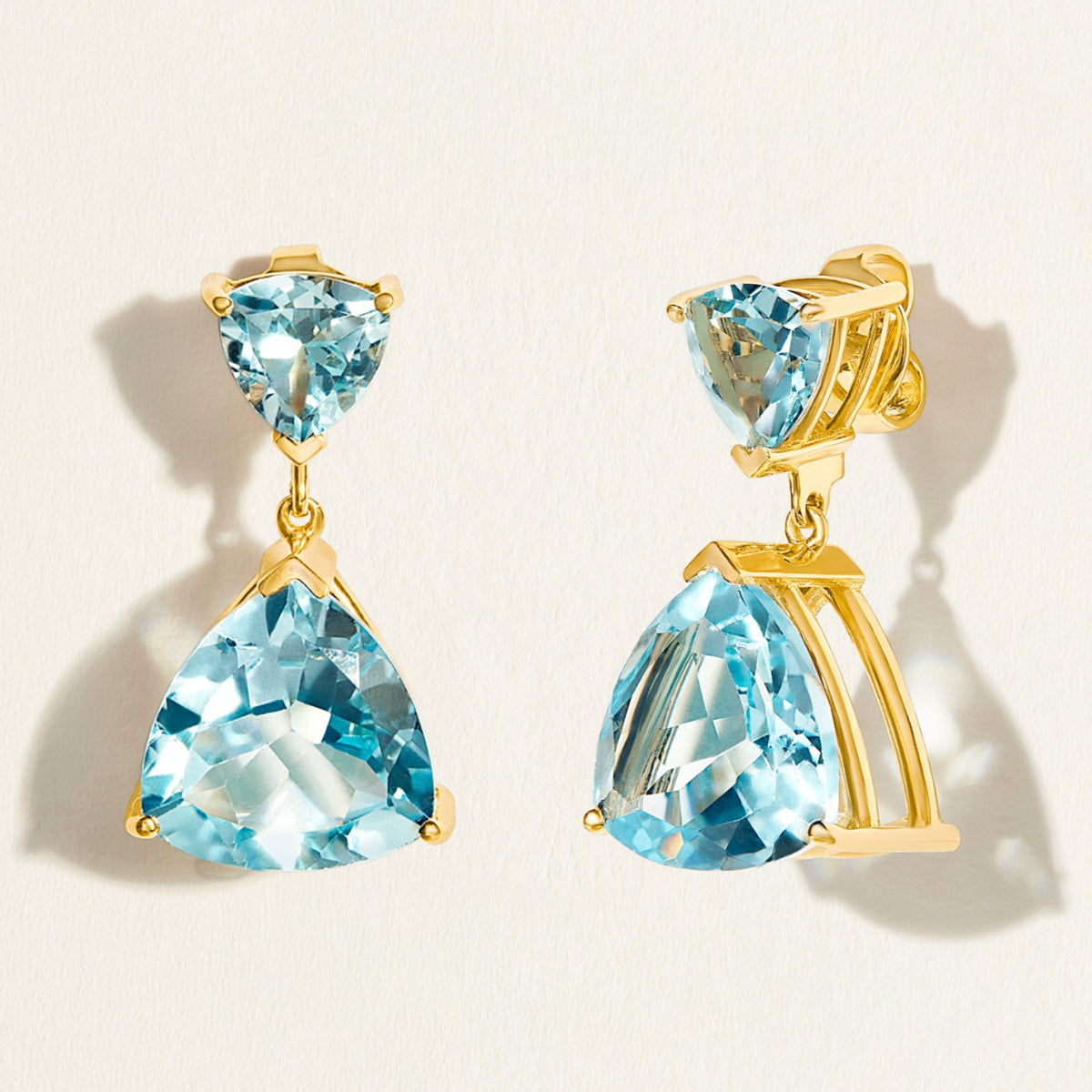 18 k Gold earrings with swiss blue topaz gemstones in triangle shape on a light beige background