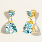 18 k Gold earrings with swiss blue topaz gemstones in triangle shape on a light beige background